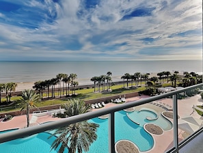 Un área de piscina con múltiples fuentes, vista a la playa y palmeras.