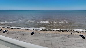 Een kustgezicht met een verharde promenade langs het strand, die naar de zee leidt.
