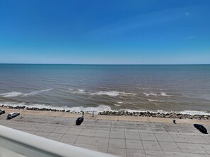 Een kustgezicht met een verharde promenade langs het strand, die naar de zee leidt.