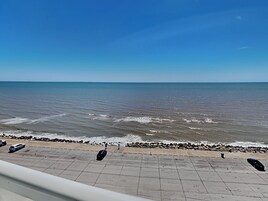 A coastal view with a paved walkway along the beach, leading to the sea.