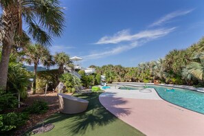 A pool area with palm trees, lounge chairs, and a covered seating area.