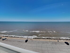 Een kustgezicht met een verharde promenade langs het strand, die naar de zee leidt.