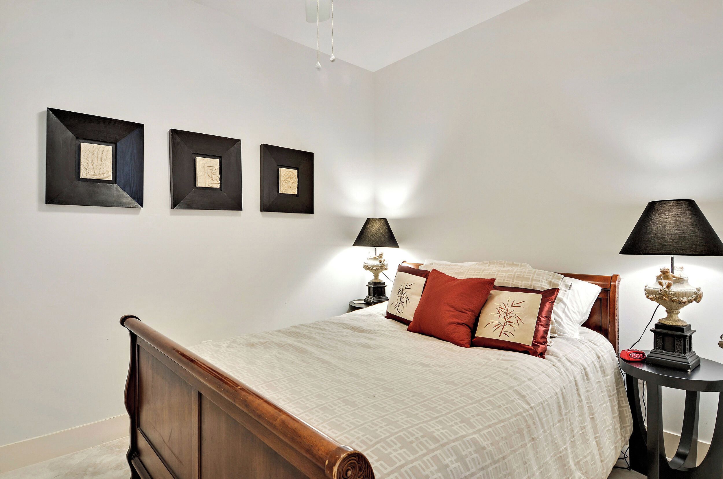 A bedroom with a wooden bed, two bedside tables with lamps, and three framed artworks on the wall.