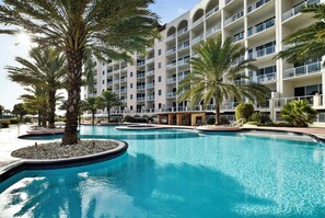 Un hôtel doté de nombreux balcons, d’une piscine bordée de palmiers et offrant une vue sur un ciel dégagé.