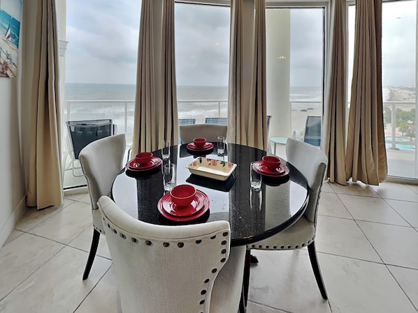 A dining area with a table set for four, large windows with curtains, and a view of the ocean.