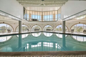 Une piscine intérieure offrant une vue dégagée sur l’extérieur, de grandes fenêtres et un plafond carrelé.