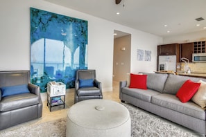 A modern living room with a grey sofa, two leather armchairs, a large abstract painting, and a kitchen area with a microwave and refrigerator.
