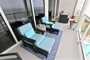 A balcony with two blue cushioned chairs, a small round table, and a potted plant.