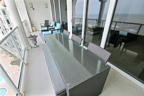 A balcony with a glass-top table and chairs, a potted plant, and a view of the ocean. - Pelican Pass by Ryson Vacation Rentals (Galveston)