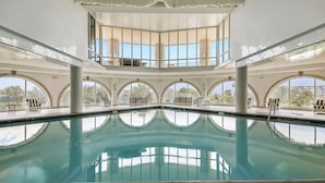 Une piscine intérieure offrant une vue dégagée sur l’extérieur, de grandes fenêtres et un plafond carrelé.