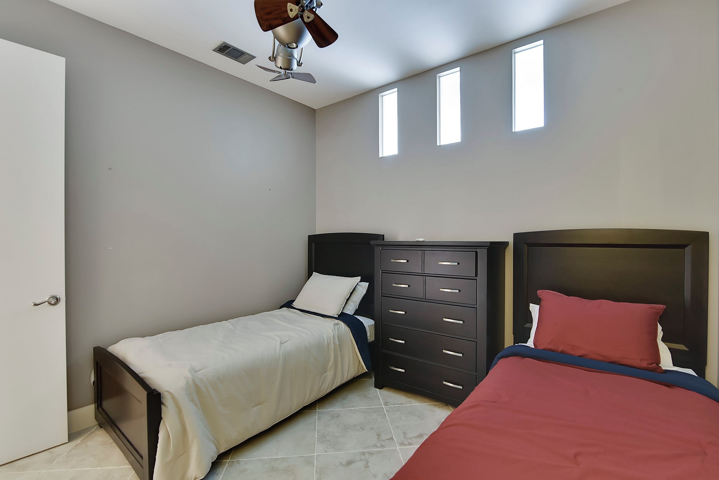 A bedroom with a single bed, a dresser, a ceiling fan, and a window.
