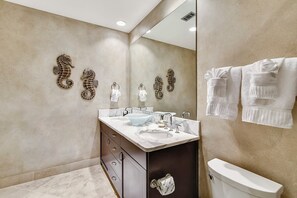 A bathroom with a marble vanity, two sinks, a toilet, and decorative seahorse wall art.
