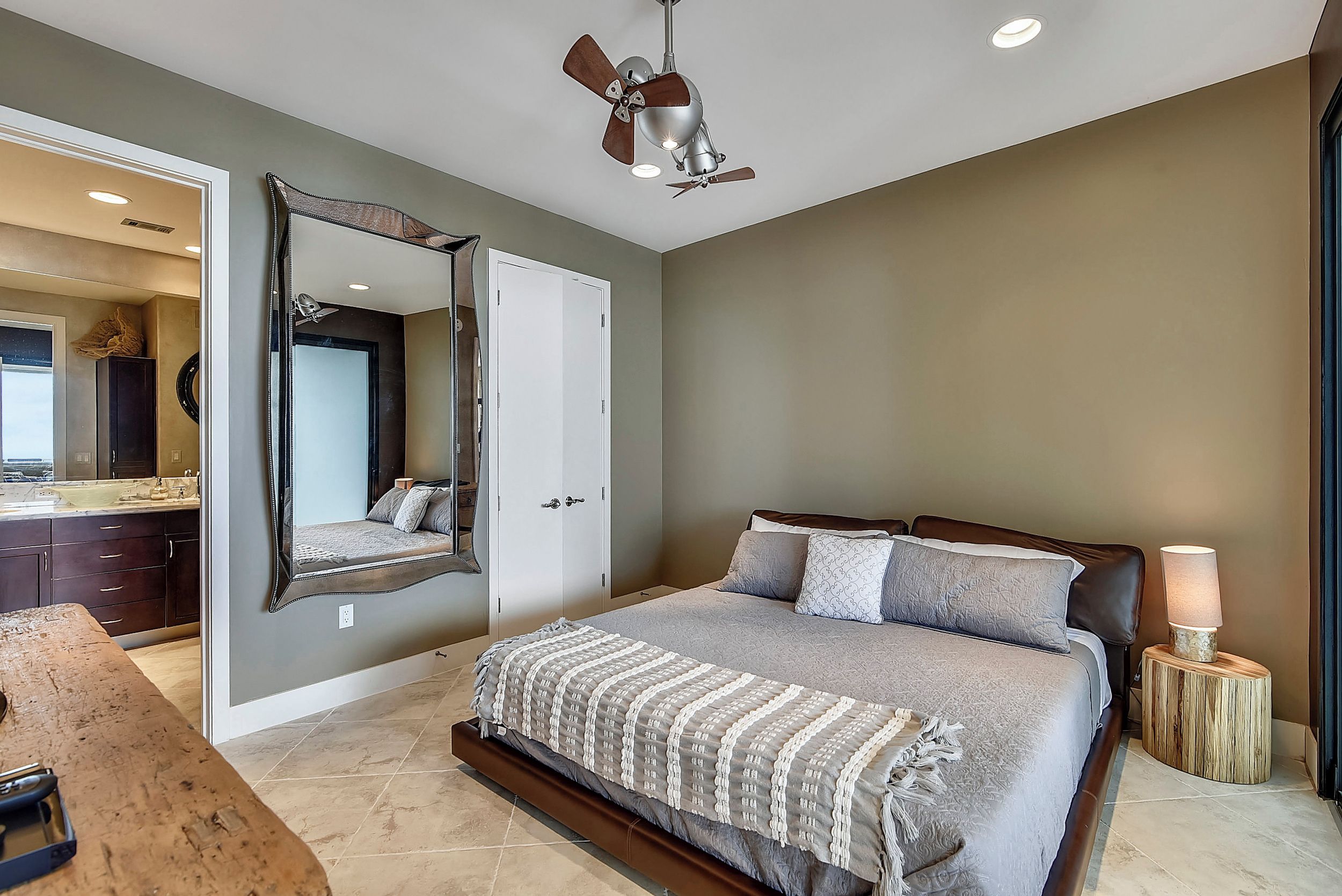 A bedroom with a bed, a ceiling fan, a bedside lamp, and a large mirror.