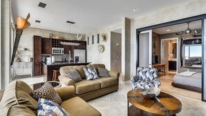 A modern living room with a sofa, armchair, and coffee table. A kitchen with a microwave and cabinets is visible in the background. - Kohinoor by Ryson Vacation Rentals (Galveston)