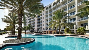 Un hôtel doté de nombreux balcons, d’une piscine bordée de palmiers et offrant une vue sur un ciel dégagé.