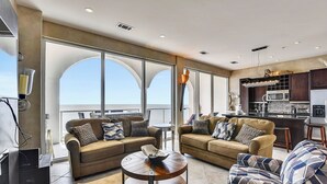 A spacious living area with two sofas, a coffee table, and a kitchen area with modern appliances. - Kohinoor by Ryson Vacation Rentals (Galveston)
