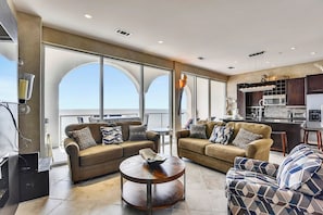 A spacious living area with two sofas, a coffee table, and a kitchen area with modern appliances. - Kohinoor by Ryson Vacation Rentals (Galveston)