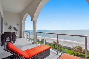 A balcony with wicker furniture and orange cushions, overlooking a beach and ocean. - Kohinoor by Ryson Vacation Rentals (Galveston)