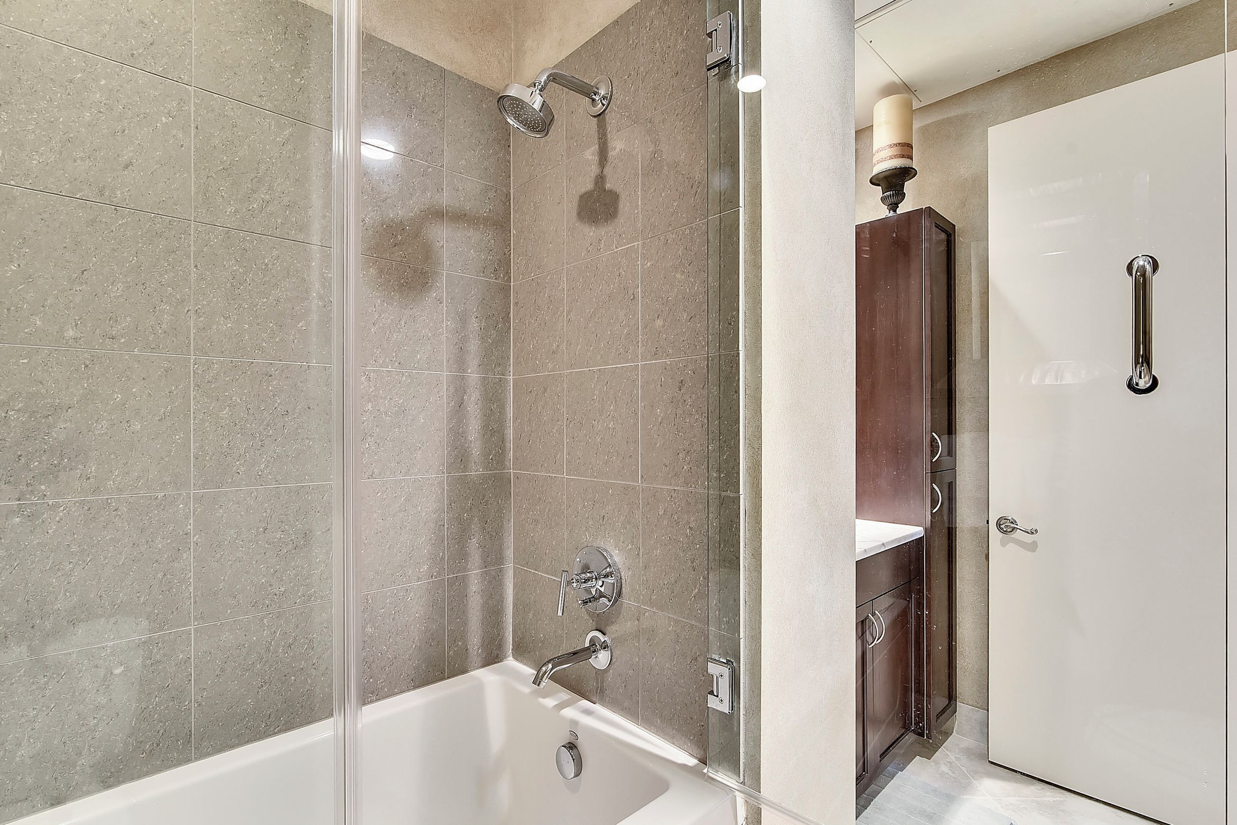 A modern bathroom with a glass-enclosed shower, a white bathtub, and a wooden cabinet with a mirror.