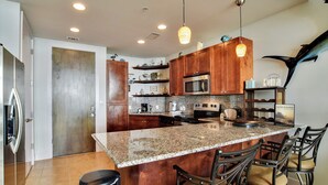 A modern kitchen with granite countertops, wooden cabinets, stainless steel appliances, and a bar area with stools. - Emerald 1111 by Ryson Vacation Rentals (Galveston)
