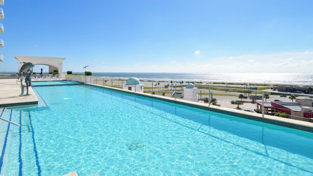 A swimming pool with clear blue water, a white gazebo, and a view of the beach and ocean. - Emerald 1111 by Ryson Vacation Rentals (Galveston)