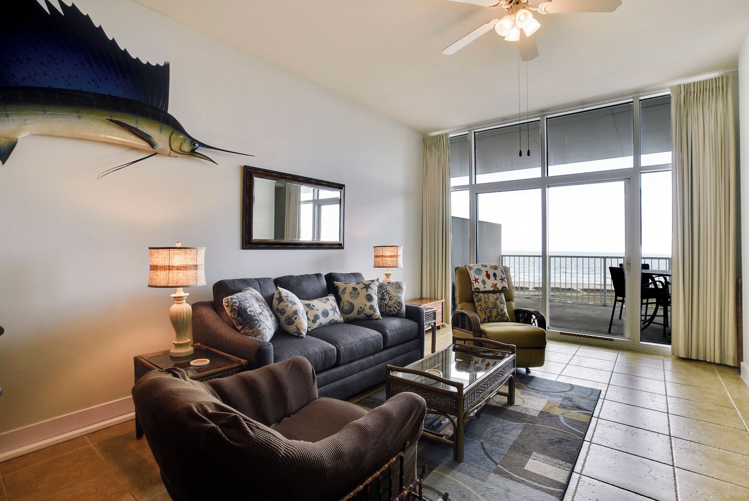 A living room with a sofa, armchair, and coffee table, a large mirror, and a ceiling fan.