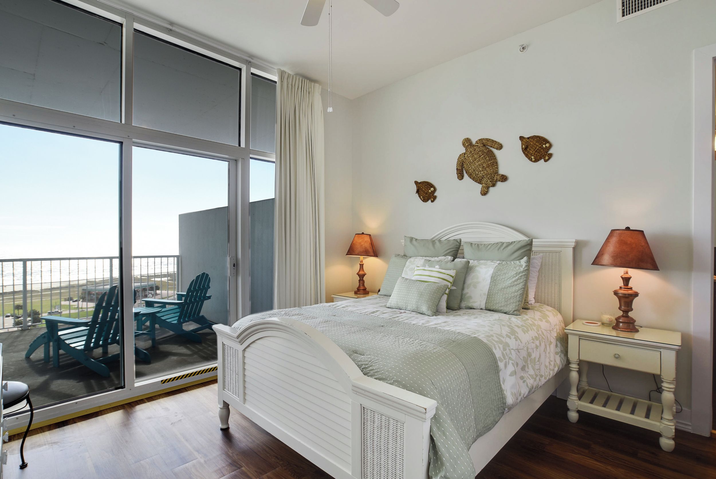 A bedroom with a large window, a bed with a white headboard, two bedside tables with lamps, and a view of the outdoors.