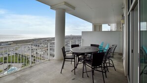 A balcony with a round table and chairs, overlooking a cityscape and the ocean. - Emerald 1111 by Ryson Vacation Rentals (Galveston)
