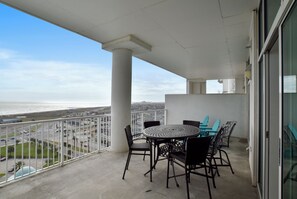 A balcony with a round table and chairs, overlooking a cityscape and the ocean. - Emerald 1111 by Ryson Vacation Rentals (Galveston)