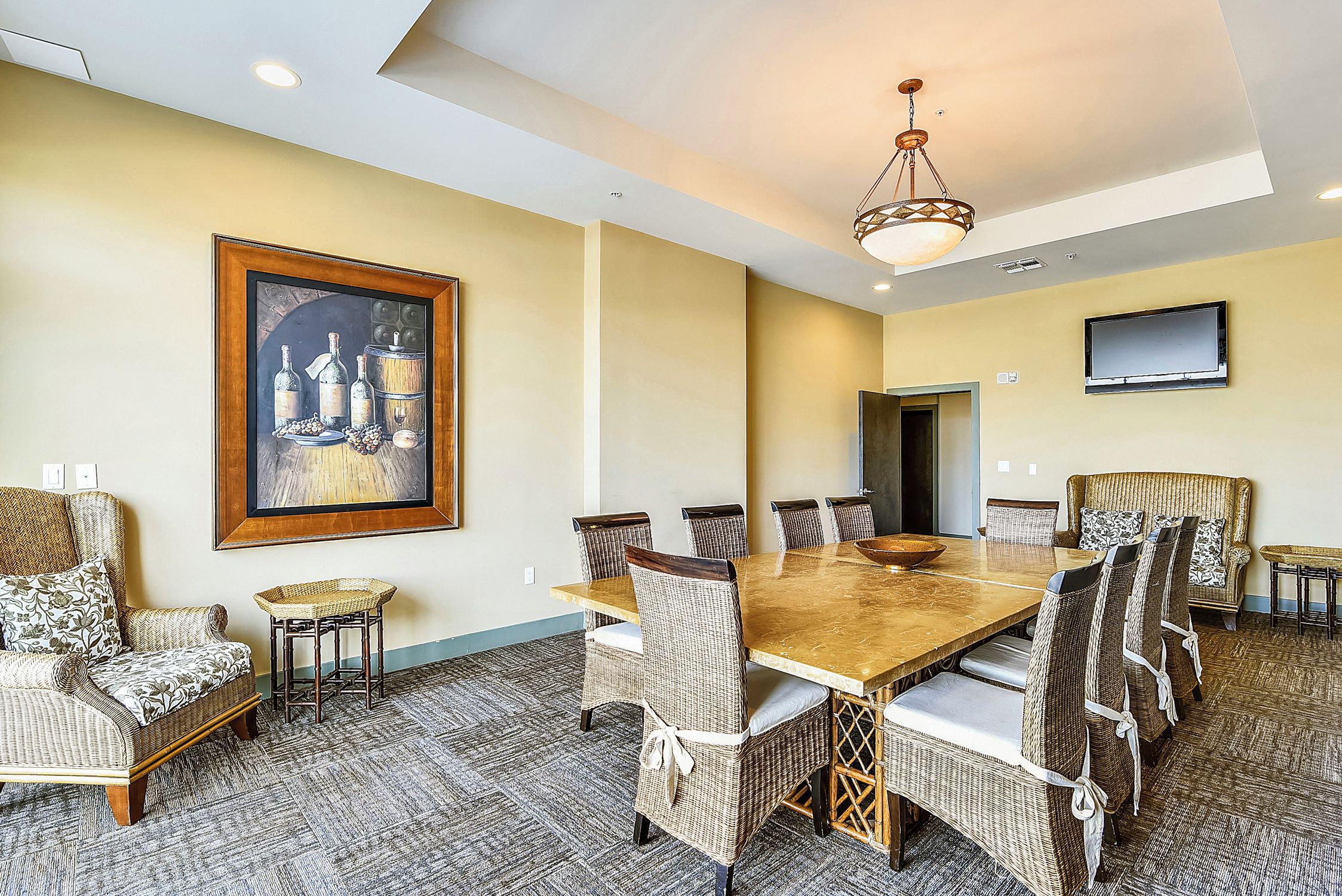 A conference room with a large table, wicker chairs, a sofa, a painting, and a TV on the wall.