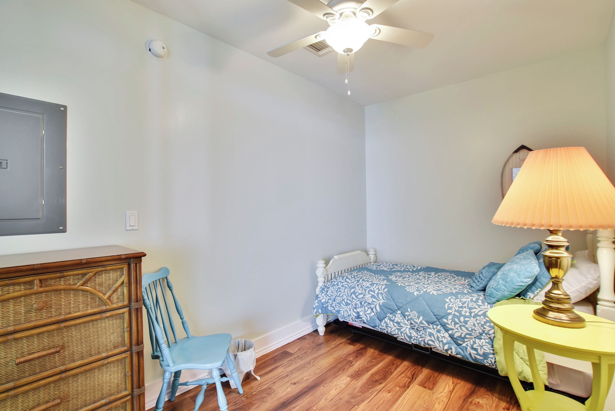 A bedroom with a bed, a chair, a dresser, a lamp, and a ceiling fan.