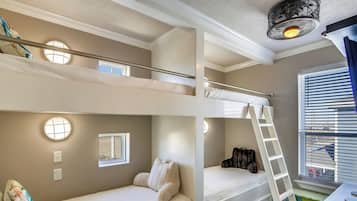 Une chambre avec des lits superposés à plusieurs niveaux, comprenant une échelle, un bureau et une fenêtre avec des stores.