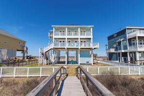 A beachfront building with a wooden boardwalk leading to a covered area with a view of the ocean.
