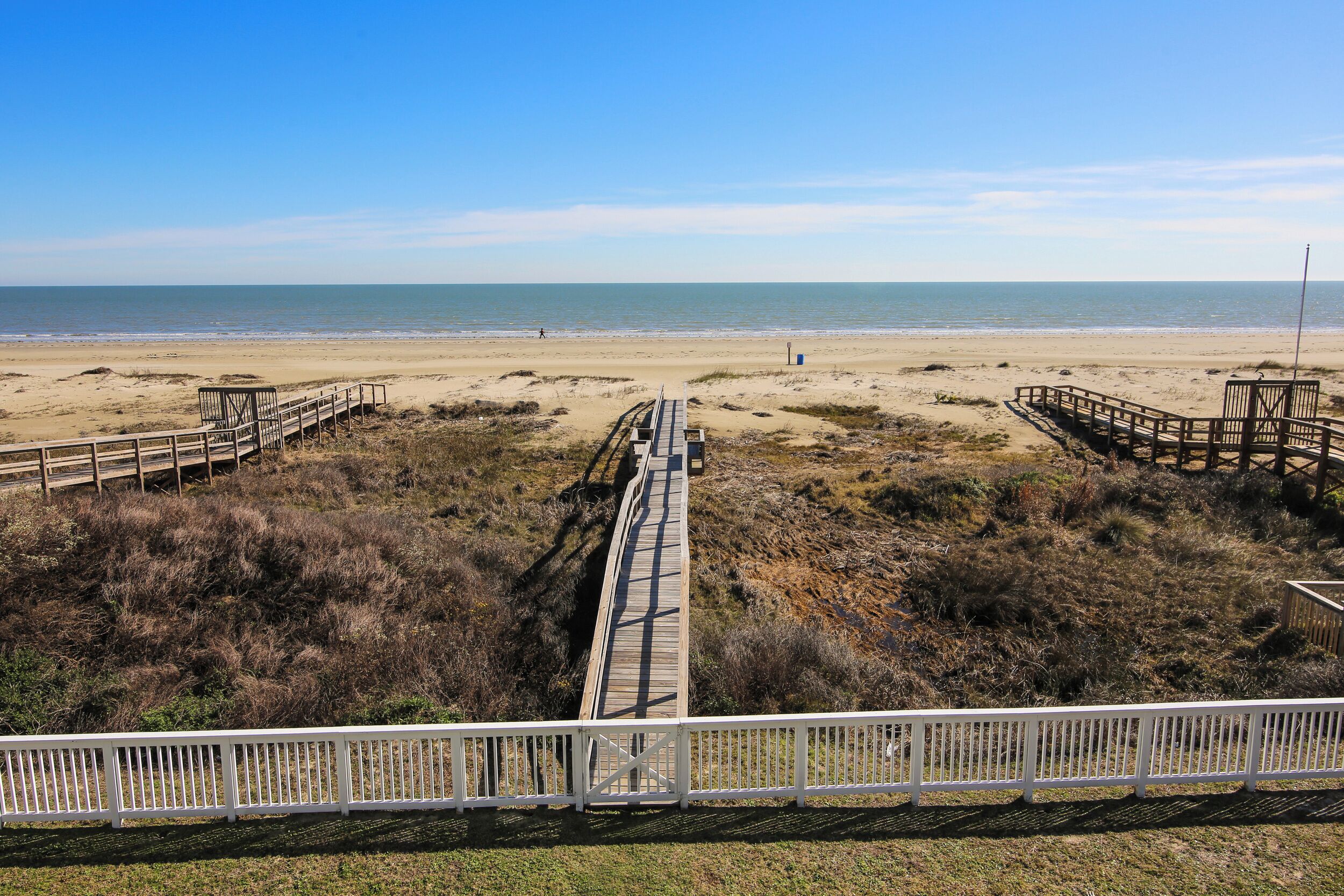 Une plage avec une promenade en bois qui mène à l’eau, entourée de dunes herbeuses.