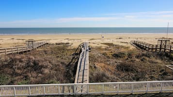 Une plage avec une promenade en bois qui mène à l’eau, entourée de dunes herbeuses.