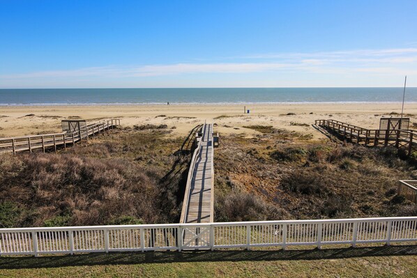 Ein Strand mit einem hölzernen Promenadenweg, der zum Wasser führt, umgeben von grasbewachsenen Dünen.