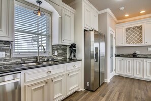 A modern kitchen with white cabinetry, a stainless steel refrigerator, and a black countertop. - Enchanted Beachfront by Ryson Vacation Rentals (Galveston)