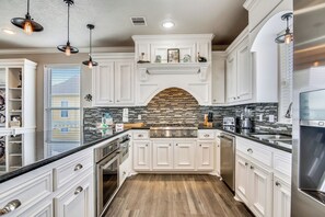 A modern kitchen with white cabinetry, a brick backsplash, and stainless steel appliances. - Enchanted Beachfront by Ryson Vacation Rentals (Galveston)