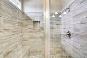 Una ducha moderna con puerta de vidrio, cabezal de ducha tipo lluvia e iluminación colgante.