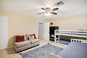 A compact living space with a sofa, a bunk bed, a ceiling fan, and a patterned rug. - Endless Summer by Ryson Vacation Rentals (Galveston)