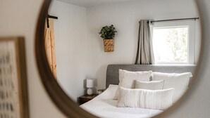 A bedroom with a bed, a bedside table, a lamp, a hanging plant, and a window with curtains.