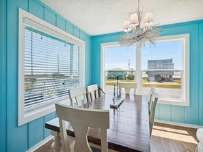 Enjoy meals in this dining area with a long table set for four, featuring a chandelier and large windows.