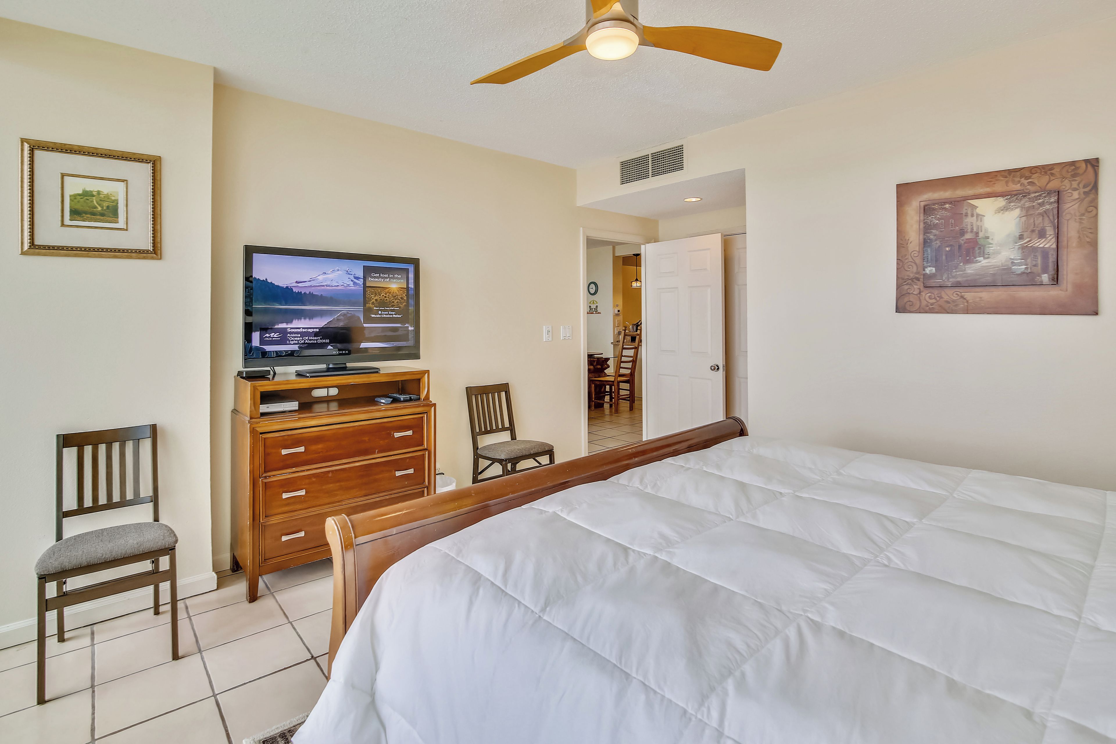 A bedroom with a bed, a TV, a dresser, and a ceiling fan.