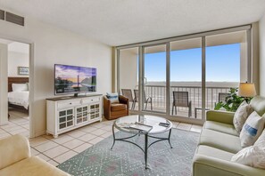 A hotel room with a large balcony, a television, a sofa, a coffee table, and a dining area. - Beachfront Getaway by Ryson Vacation Rentals (Galveston)
