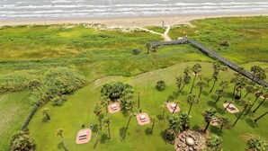 Vista aérea de un complejo turístico costero con playa, un sendero peatonal y varias zonas de estar al aire libre rodeadas de palmeras.