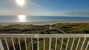 Vista costera desde un balcón con terraza de madera, playa y océano.