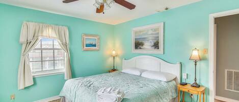 A bedroom with a bed, two bedside tables, a ceiling fan, a window with curtains, and two wall-mounted lamps.