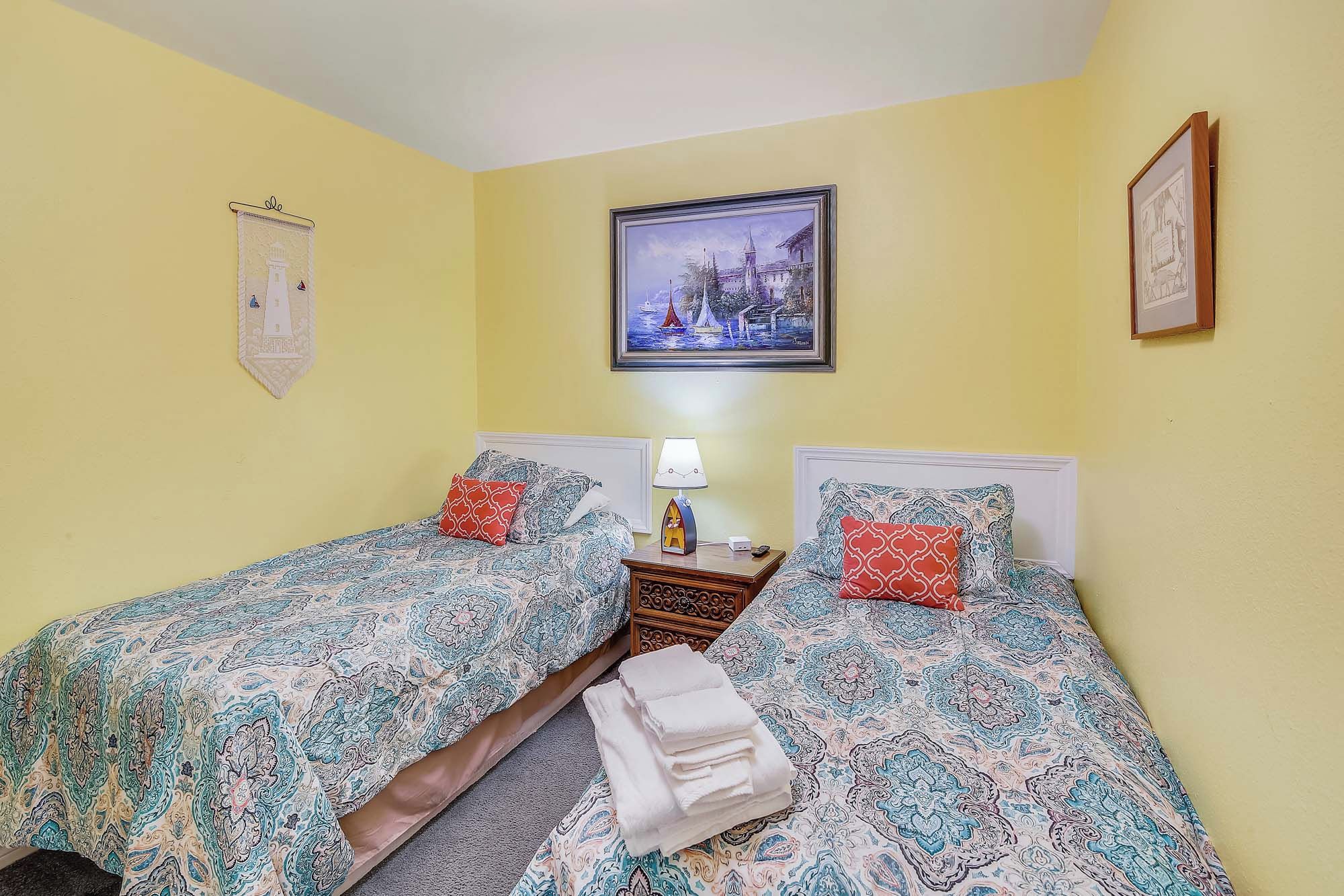 A room with two beds, a nightstand with a lamp, and a painting on the wall.