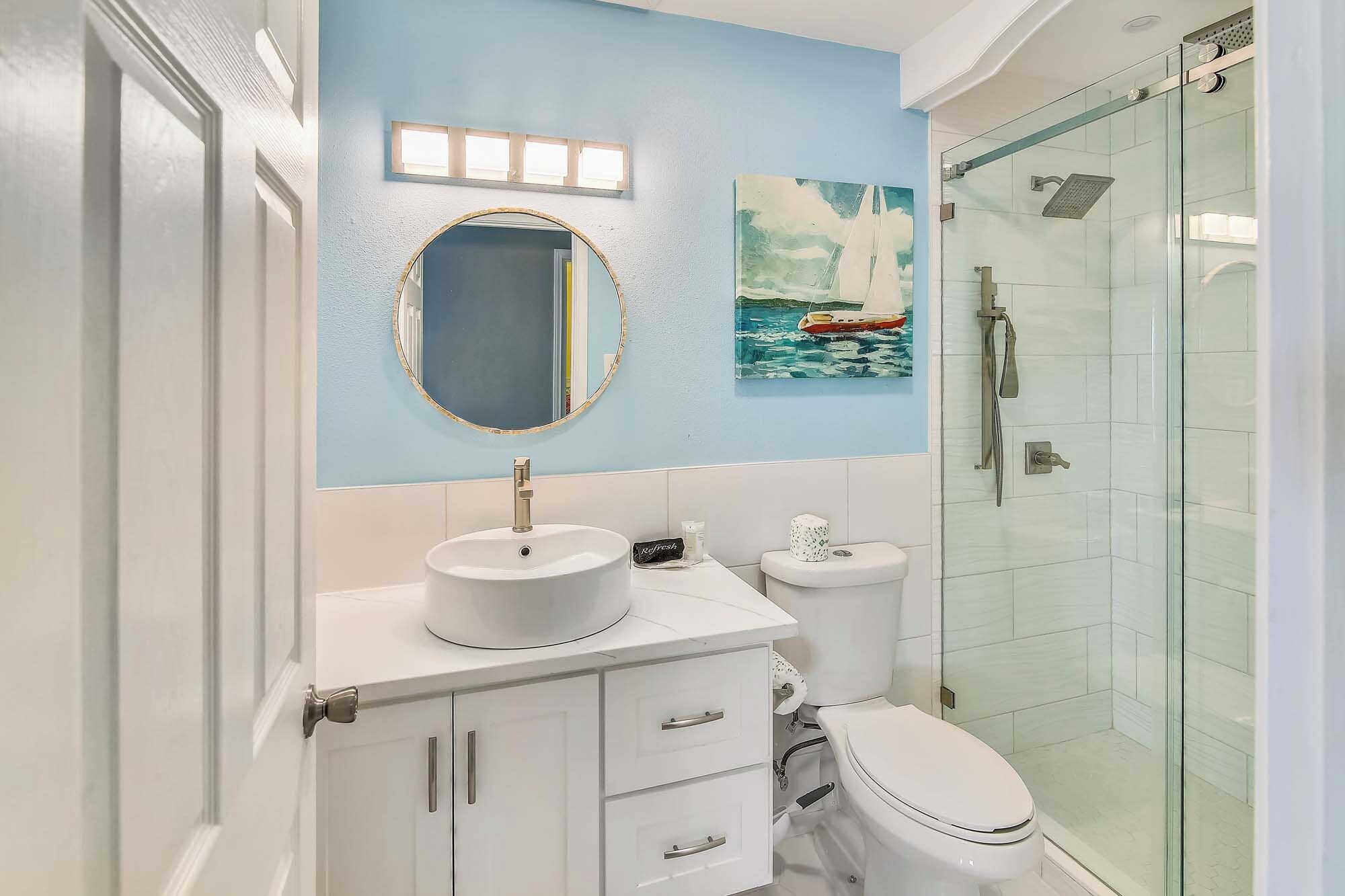 Une salle de bain avec un miroir rond, un lavabo, des toilettes et une douche à parois de verre.