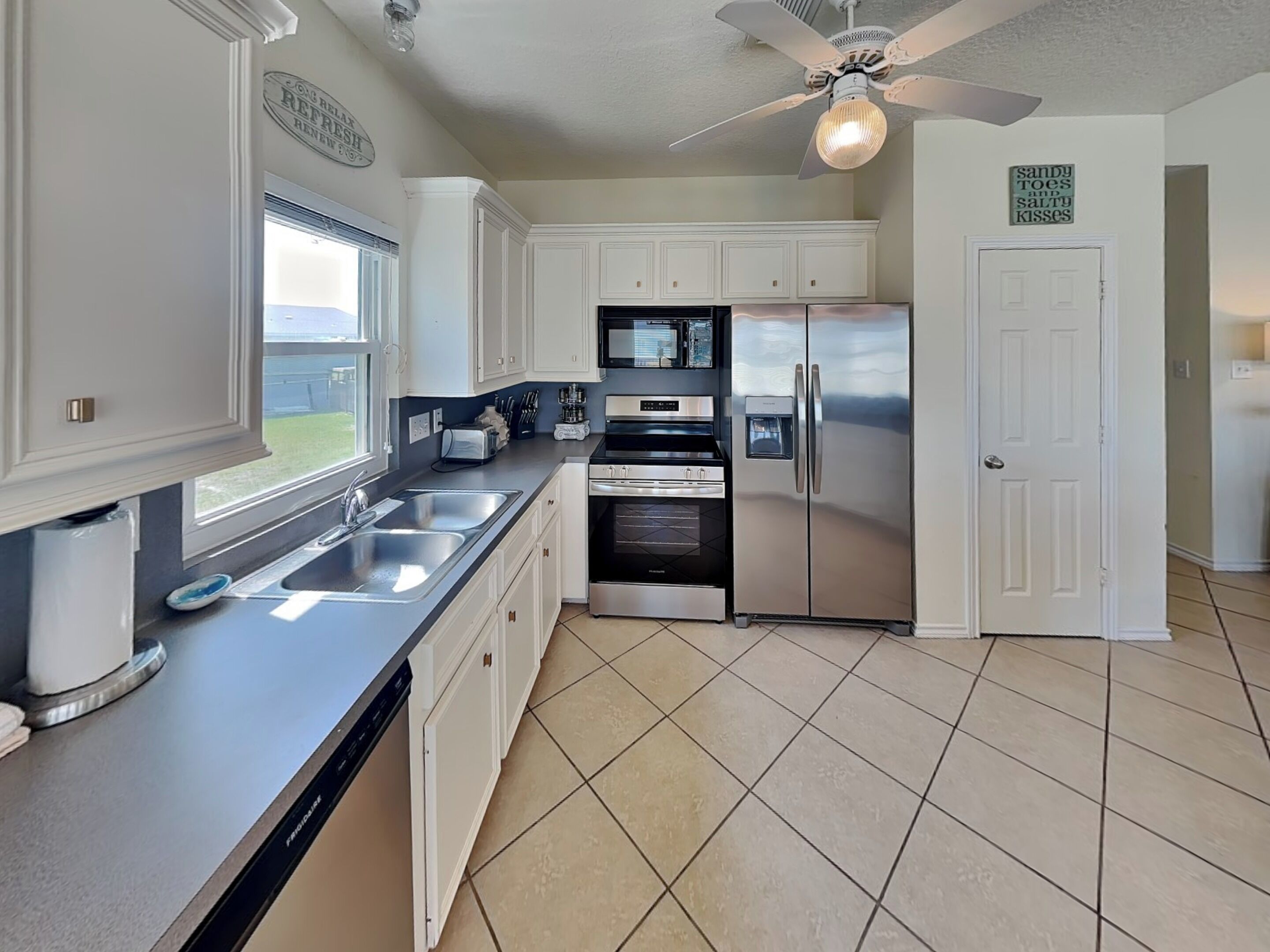 A kitchen with white cabinets, stainless steel appliances, a dishwasher, and a ceiling fan.